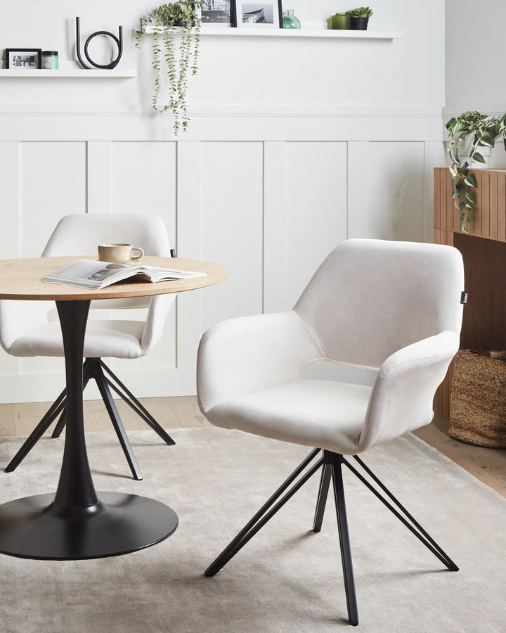 A pair of off-white swivel dining chairs arranged around a round wooden table, creating a clean and contemporary dining space with neutral tones, greenery, and modern décor accents.