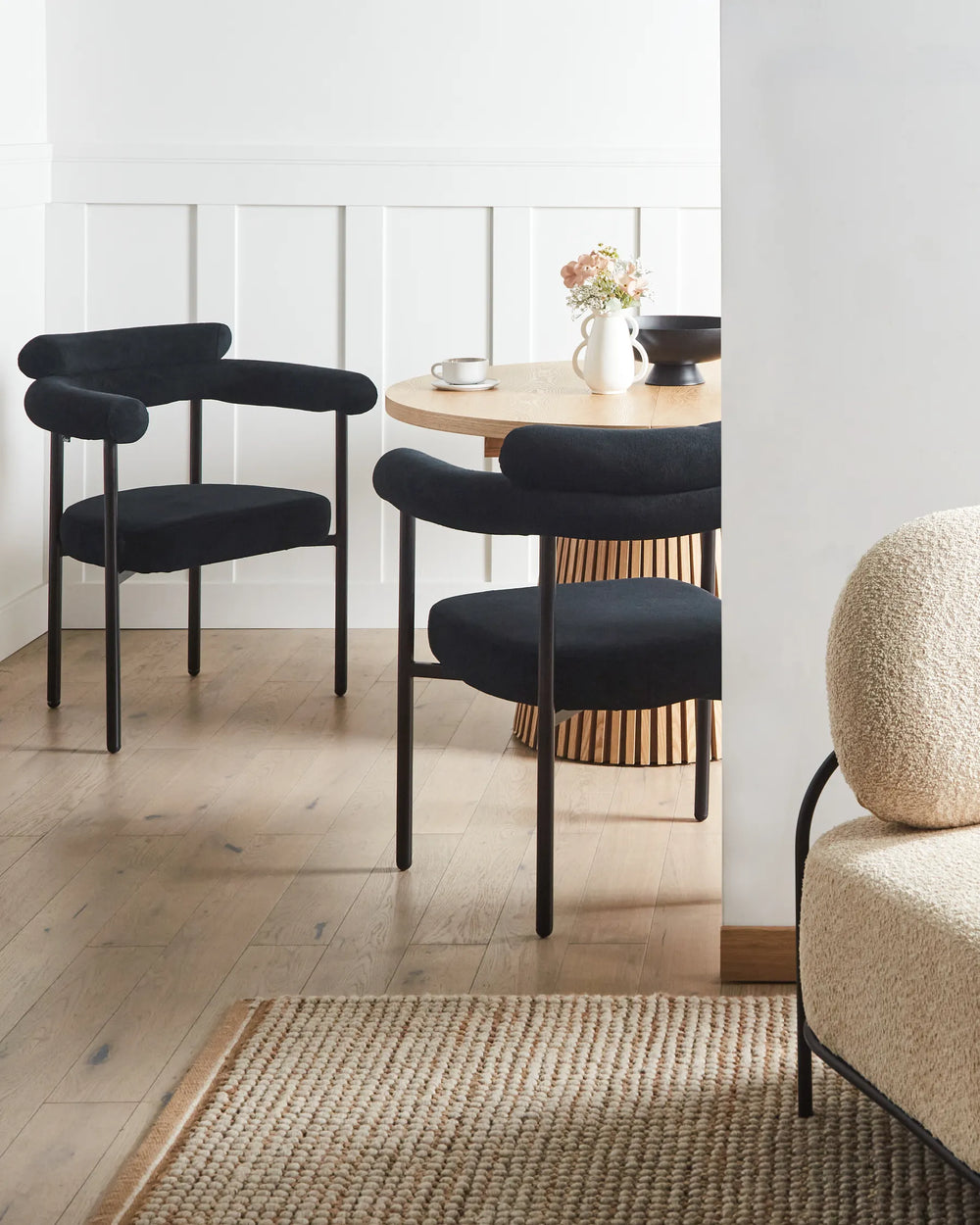 Black fabric dining chairs with rounded backrests and black metal legs arranged around a dining table in a contemporary dining space with minimalist décor.