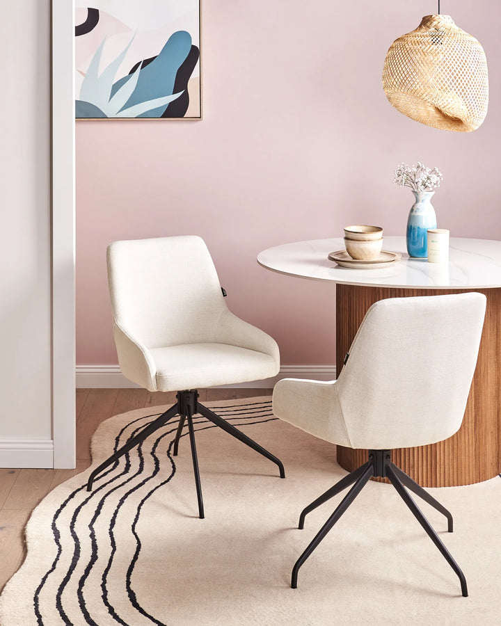 Off-white fabric swivel dining chairs with black metal bases around a dining table in a bright, modern dining space with minimalist décor.
