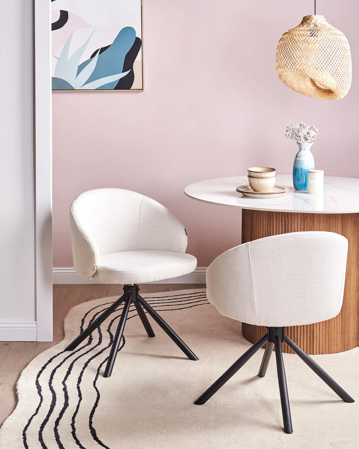 Off-white fabric swivel dining chairs with black metal bases around a dining table in a bright, modern dining space with minimalist décor.