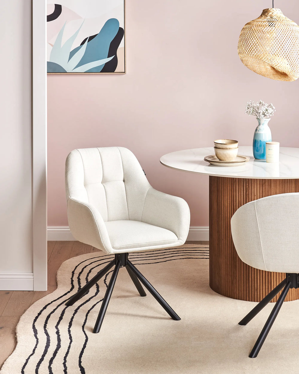 Cream swivel dining chairs around a round dining table with a pink accent wall, pendant light, and modern décor.