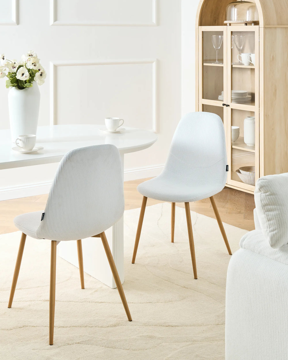 White corduroy dining chairs with wood-effect metal legs arranged around a dining table in a bright, Scandinavian-style dining space with minimalist décor.