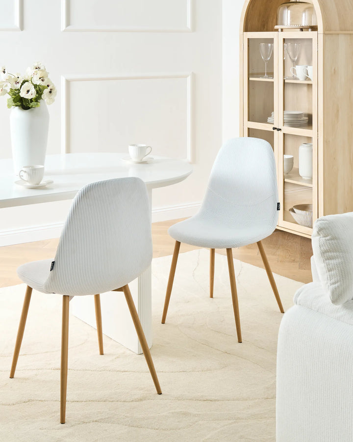 White corduroy dining chairs with wood-effect metal legs arranged around a dining table in a bright, Scandinavian-style dining space with minimalist décor.