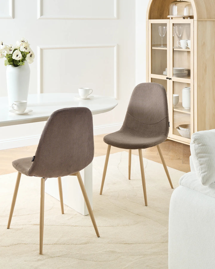 Taupe corduroy dining chairs with wood-effect metal legs arranged around a dining table in a bright, Scandinavian-style dining space with minimalist décor.
