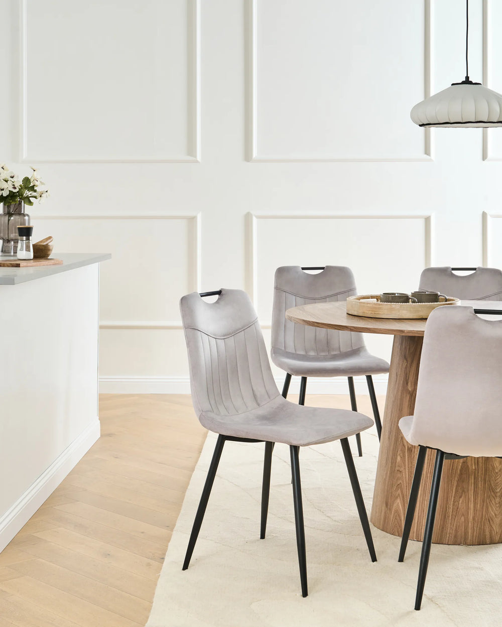 Light grey velvet dining chairs with tufted backrests and black metal legs arranged around a dining table in a modern dining space with contemporary décor.