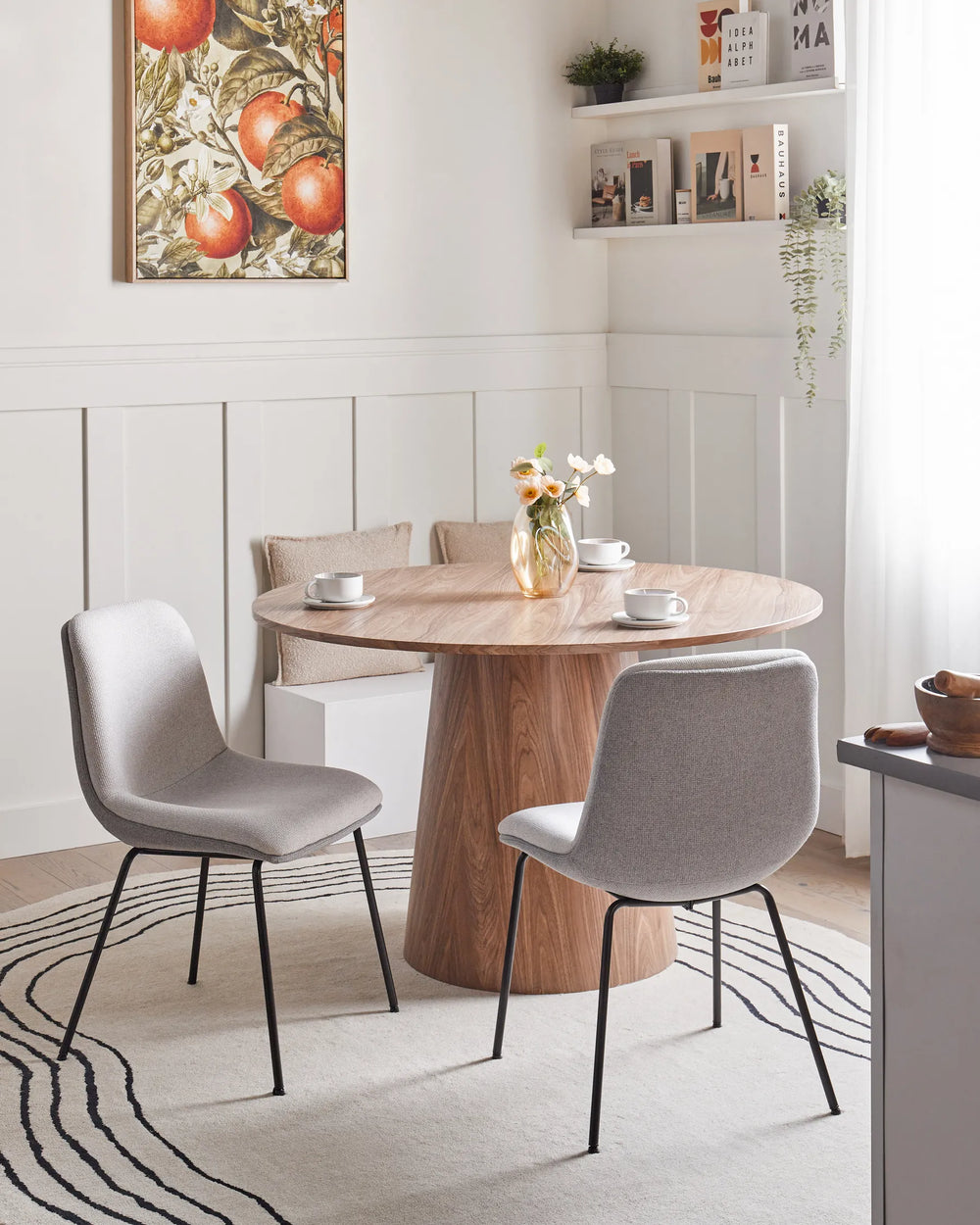 Light grey dining chairs around a round wooden table in a bright, modern dining room with neutral décor, wall art, and natural light.