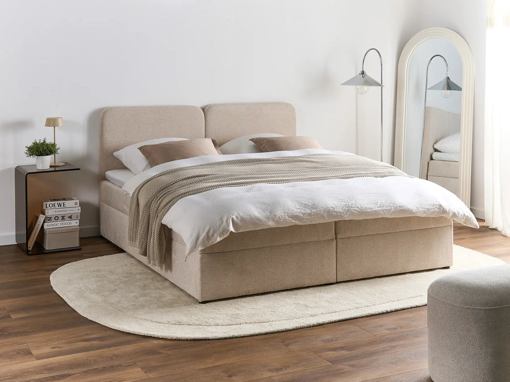 Beige upholstered bed in a bedroom setting with wooden flooring and a mirror.