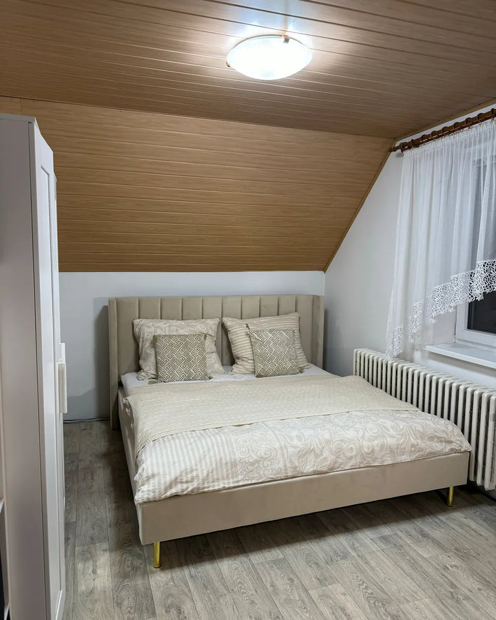 Bedroom with a bed, headboard, and pillows against a wooden ceiling.
