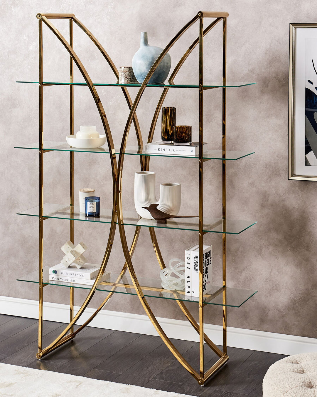 Gold metal and glass shelf against a beige wall with decorative items.