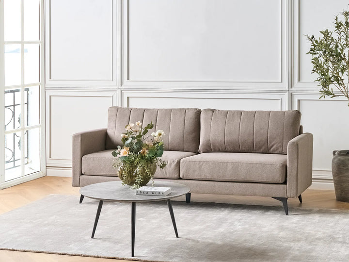 Beige sofa in a living room with a coffee table and flowers.