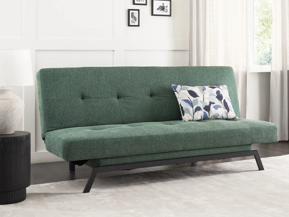 Green futon sofa with a pillow in a room with a window and curtains.