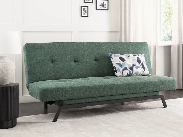 Green futon sofa with a pillow in a room with a window and curtains.
