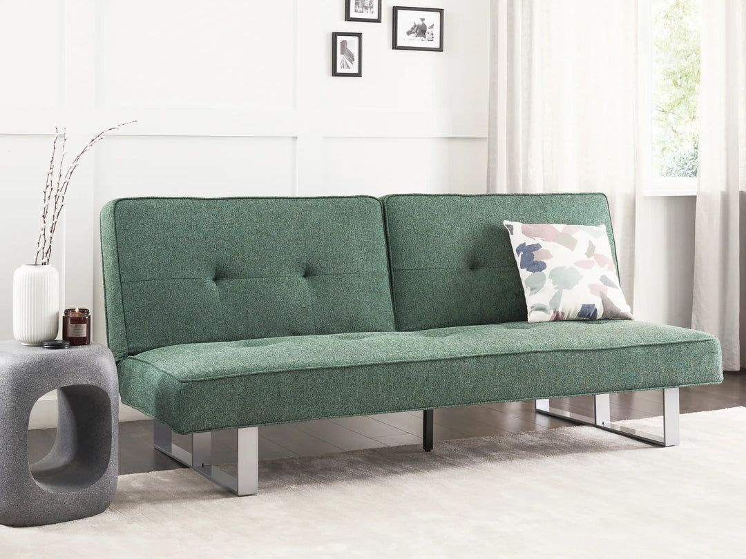 Green futon sofa in a room with a small table and decorative items.