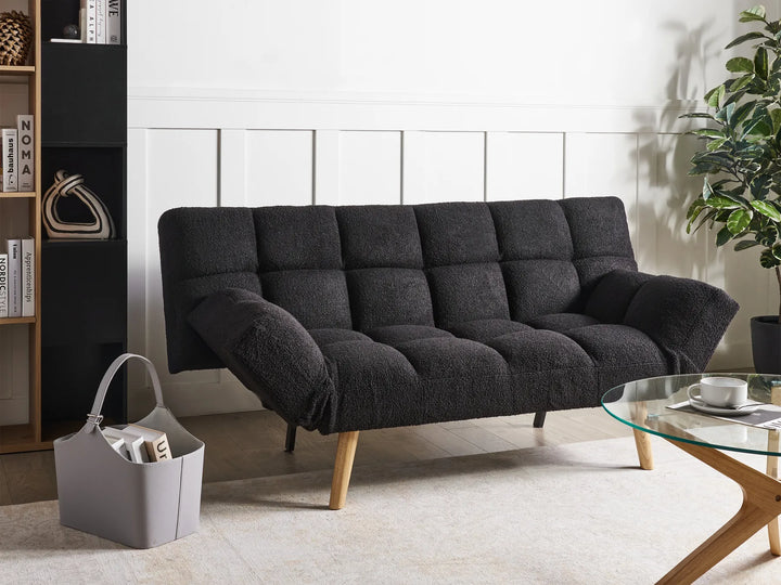 Dark gray sofa bed in a living room setting with a coffee table and plant.