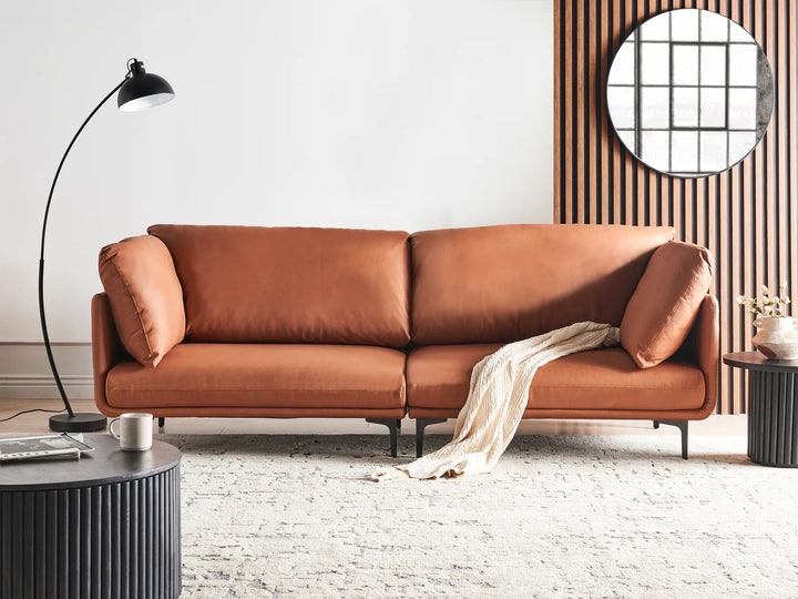 Brown leather sofa in a modern living room with a lamp and decorative items.