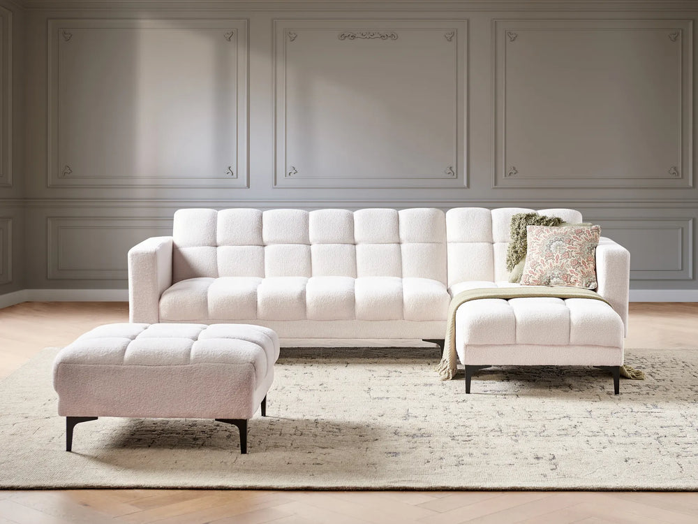 Beige sectional sofa with ottoman in a room with gray walls and a rug.