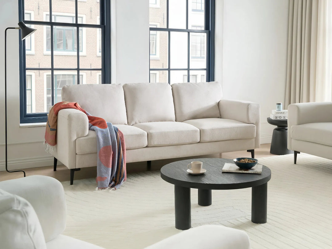 Modern living room with a beige sofa, black coffee table, and large windows.