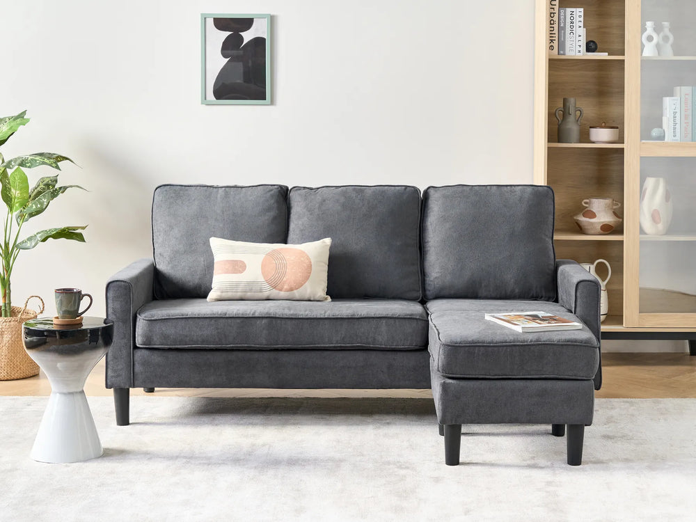 Gray sectional sofa in a living room setting with a plant and side table.