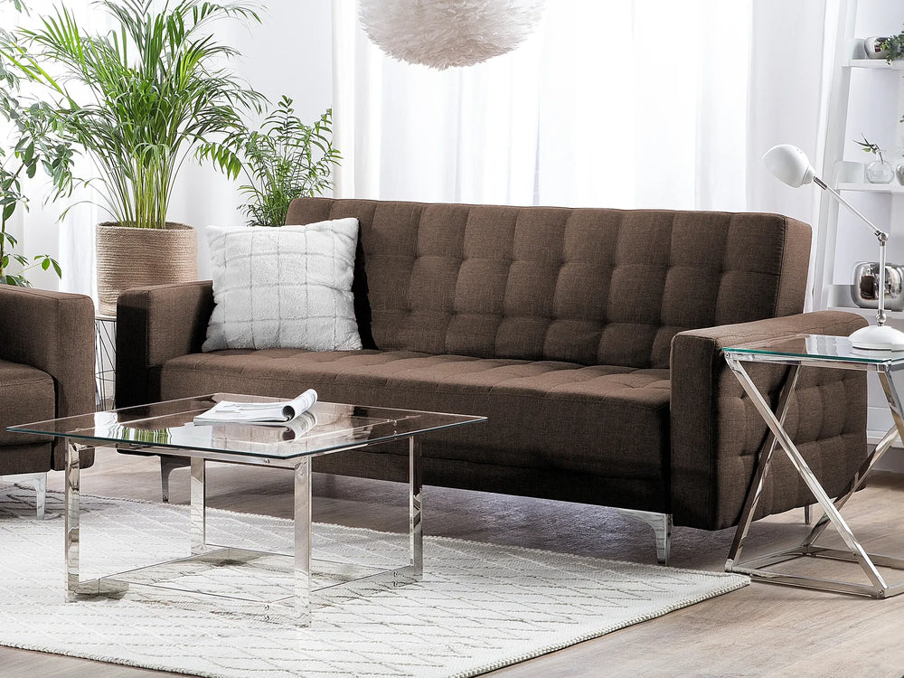 Modern living room with brown sectional sofa, glass coffee table, and decorative plants.