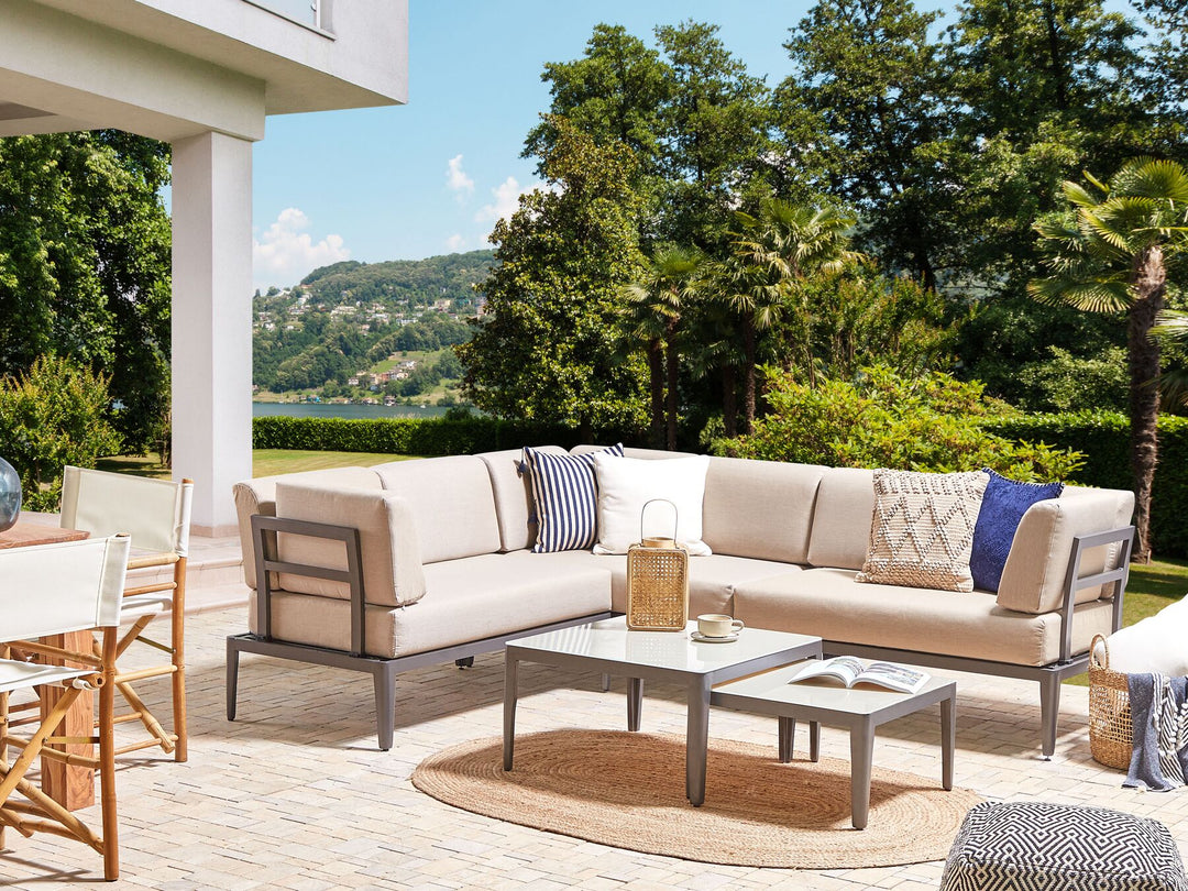 Outdoor patio with beige sectional sofa, coffee table, and chairs with a scenic background.