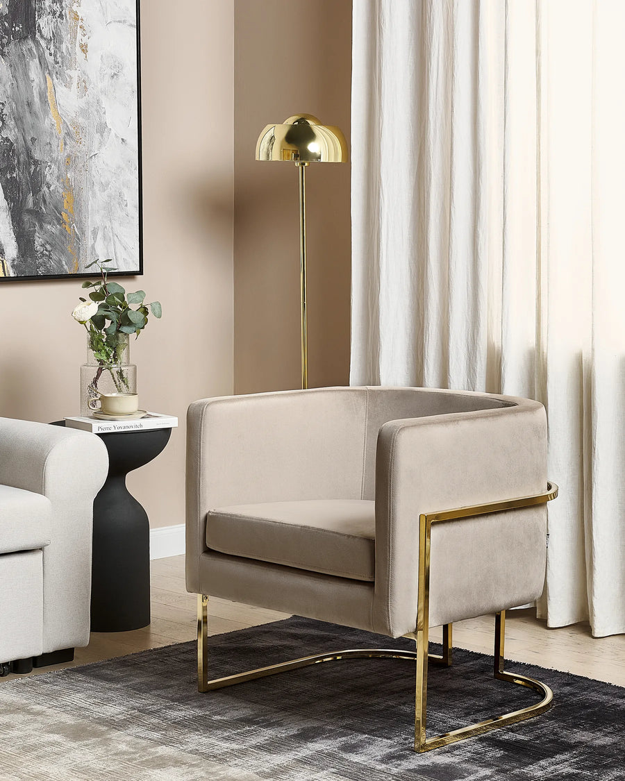 Modern living room with beige armchair, gold legs, and abstract art on wall.