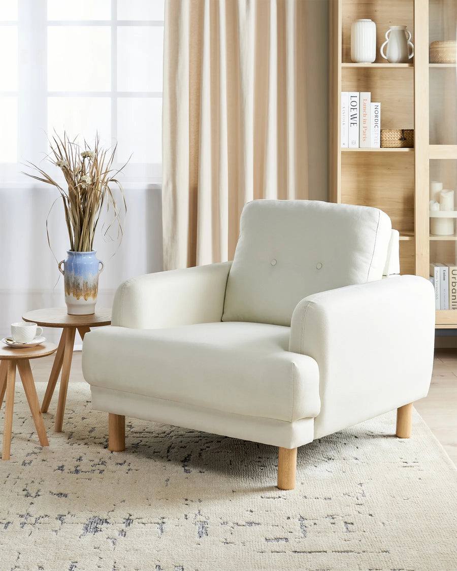 White armchair in a living room setting with a bookshelf and decorative items.