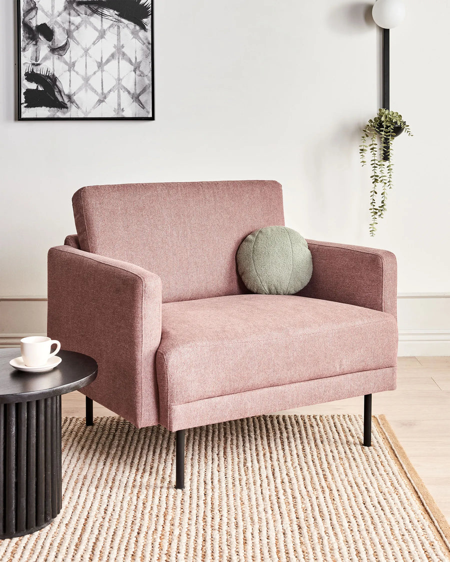 Pink armchair with a green cushion in a living room setting.