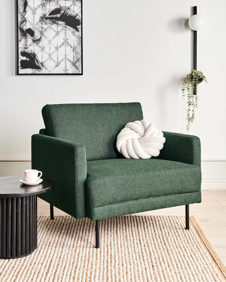 Green armchair with a decorative pillow in a modern living room setting.