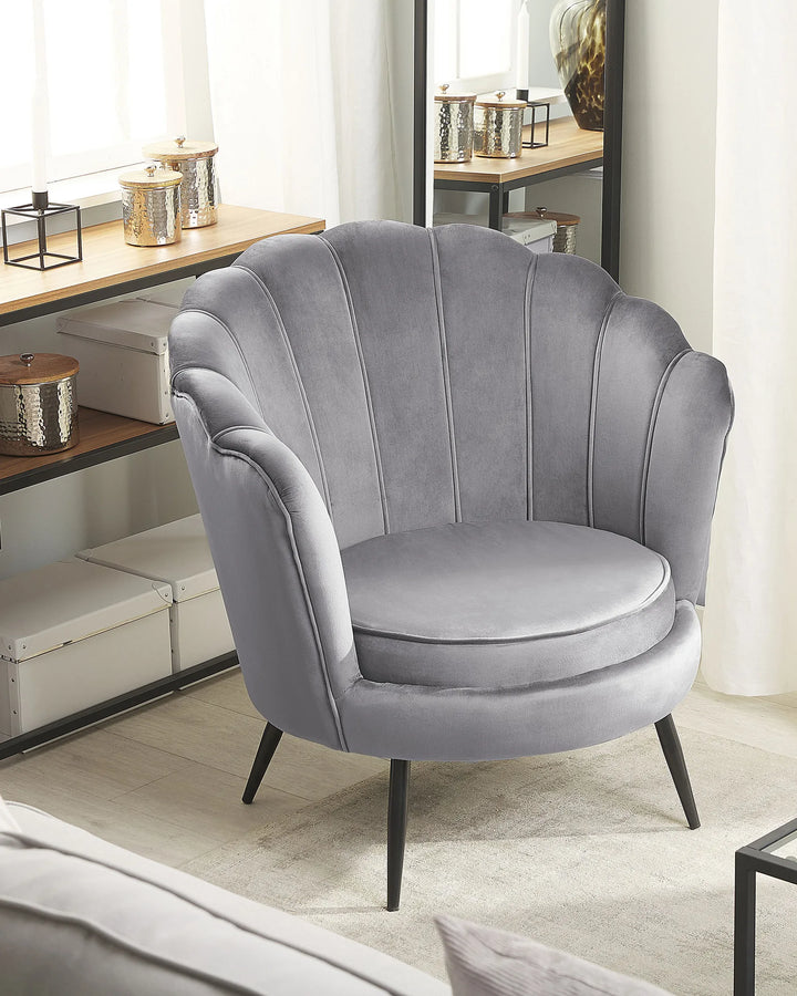 Gray velvet armchair in a room with a desk and decor items.