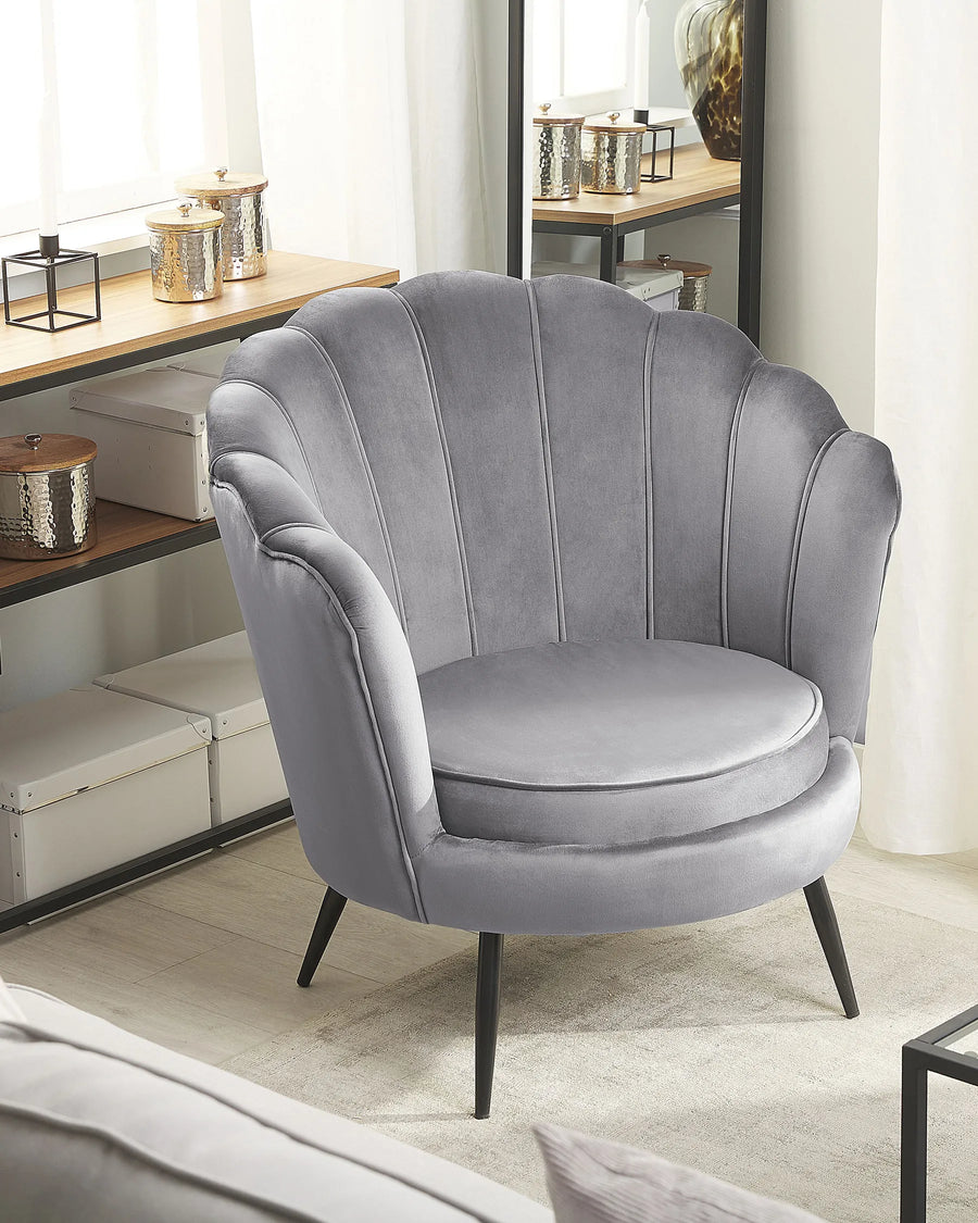 Gray velvet armchair in a room with a desk and decor items.