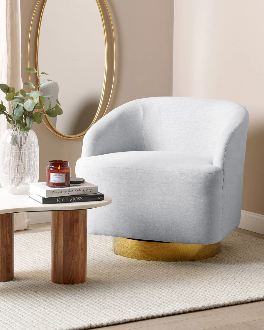 Gray swivel chair with gold base in a room with a round mirror and small table.