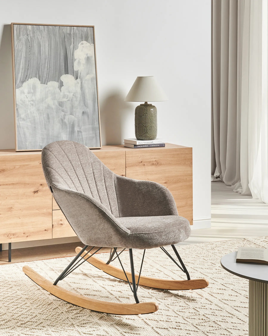Gray rocking chair in a modern living room with wooden furniture and abstract art.