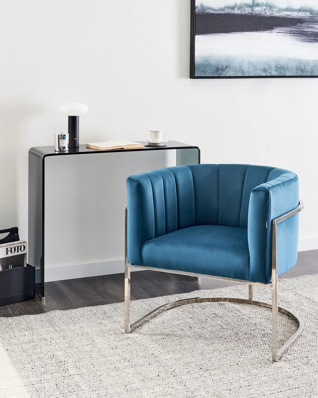 Blue armchair in a modern living room setting with a console table and artwork on the wall.