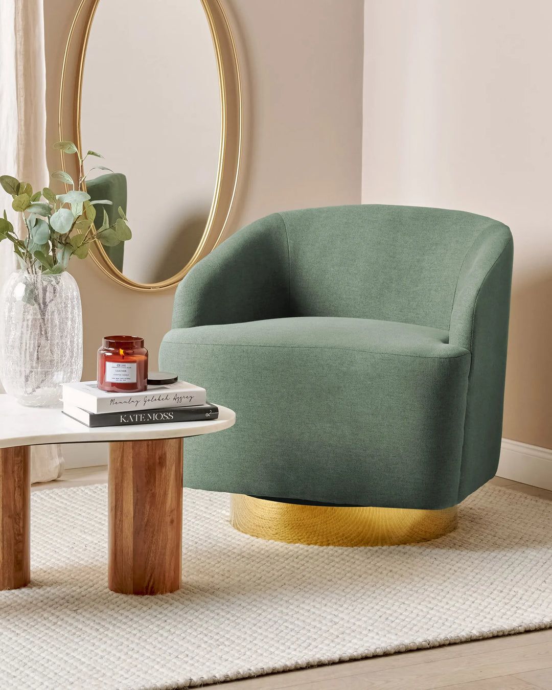 Green armchair with gold base in a room setting with a mirror and small table.