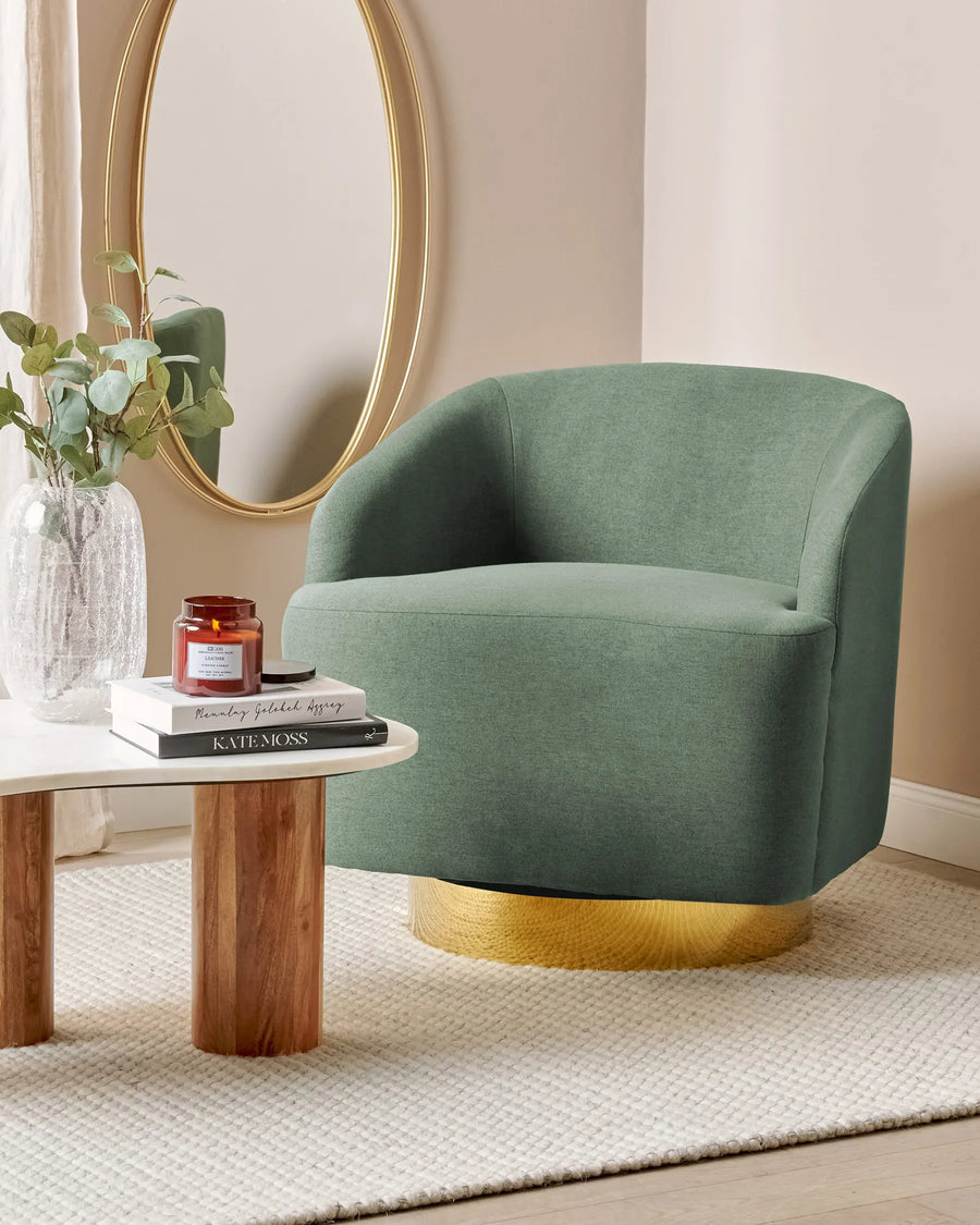 Green armchair with gold base in a room setting with a mirror and small table.