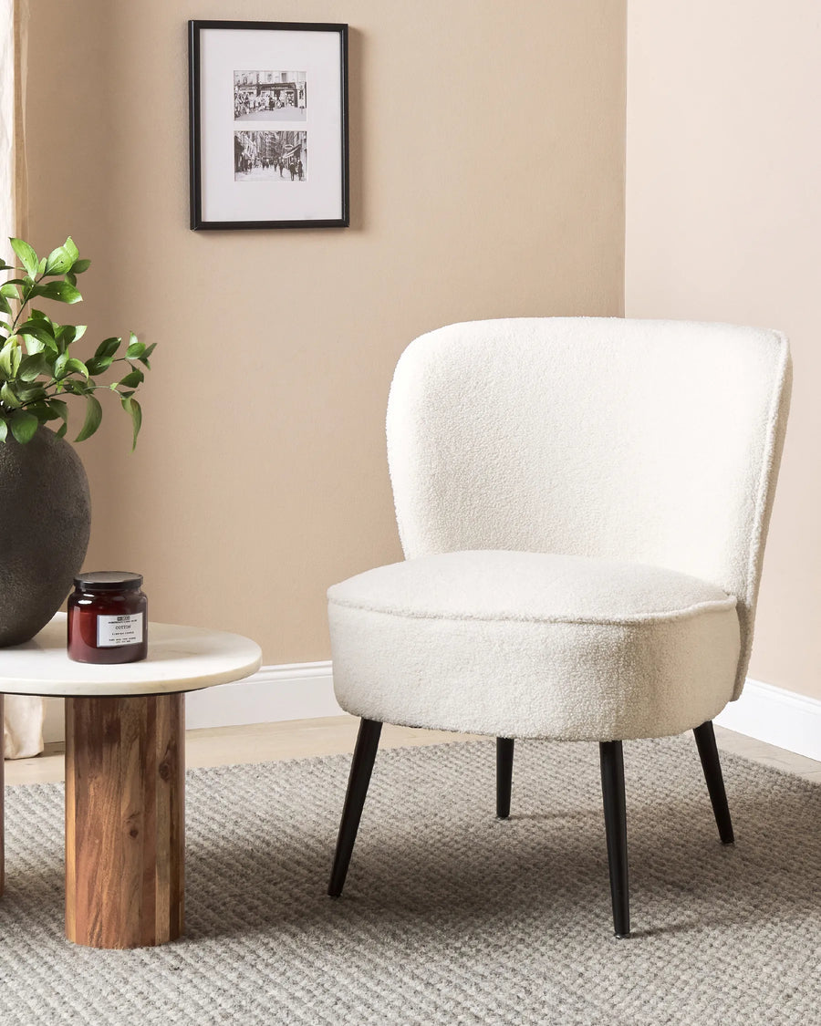 White upholstered chair in a room with a wooden side table and plant