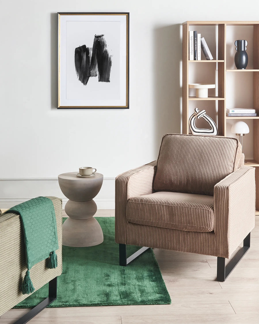 Modern living room with a brown armchair, green rug, and bookshelf.