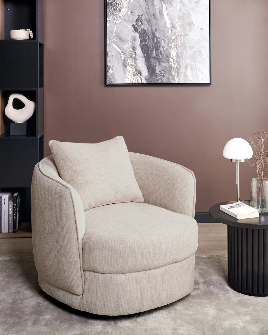 Beige armchair in a living room setting with a bookshelf and table in the background.