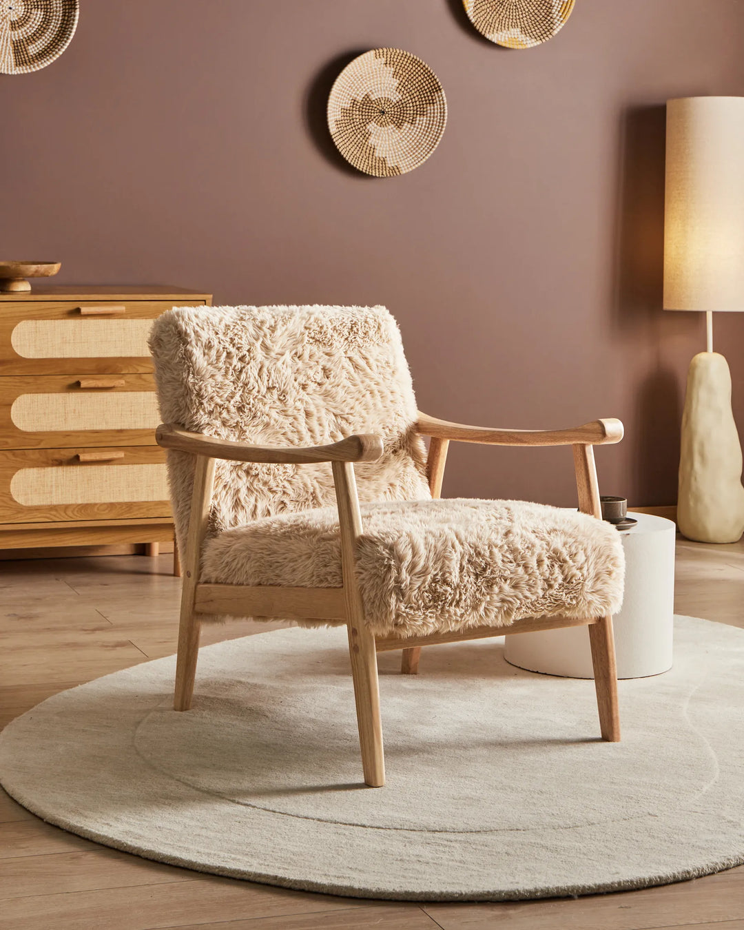 Beige armchair with wooden frame in a room with a brown wall, wooden dresser, and round rug.