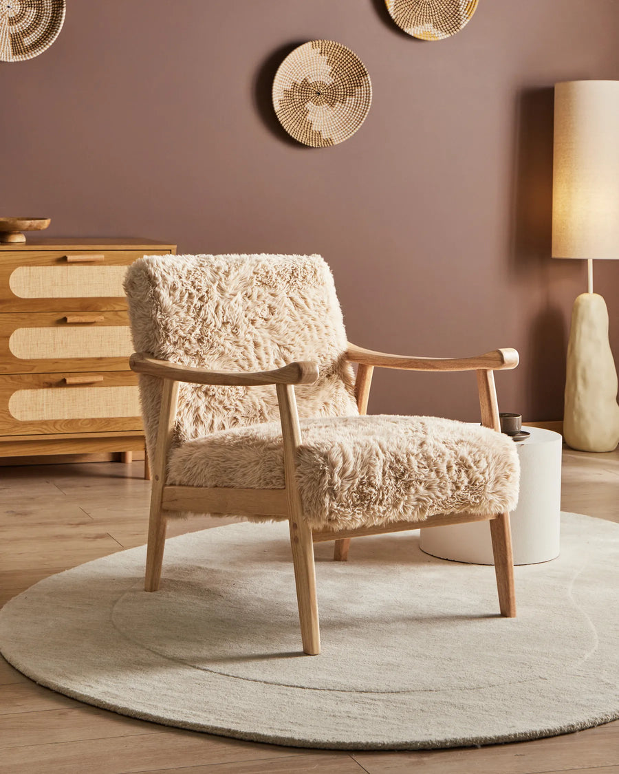 Beige armchair with wooden frame in a room with a brown wall, wooden dresser, and round rug.