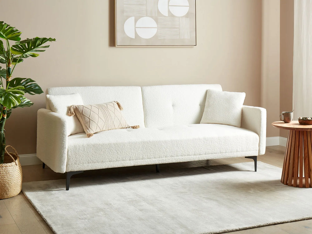 White sofa in a living room with a plant and small table.