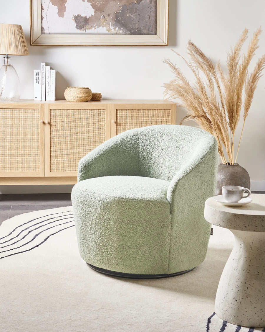 Green armchair in a room with a wooden cabinet, books, and decorative items.