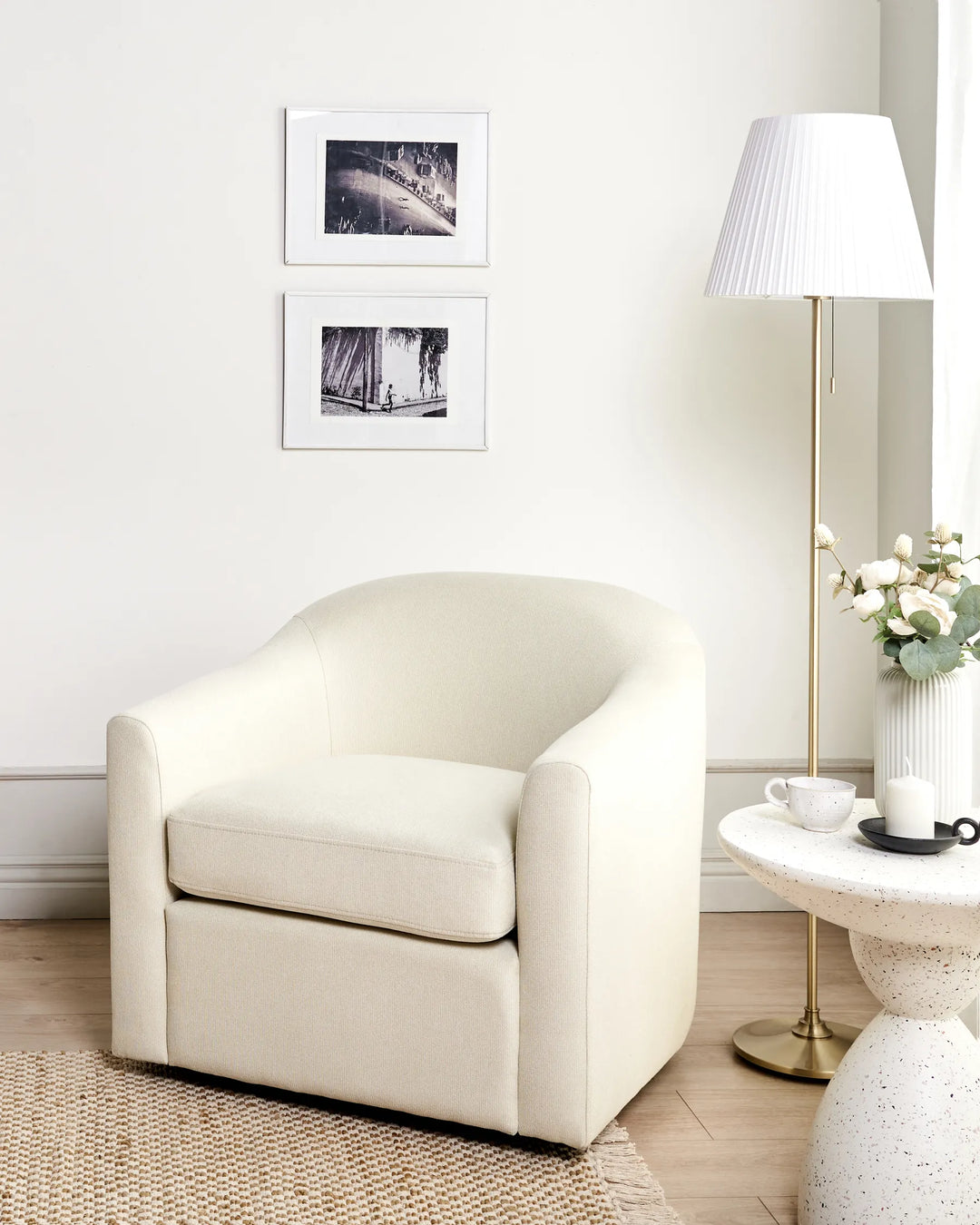 White armchair in a room with a lamp, table, and framed pictures on the wall.