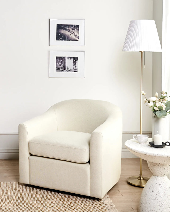 White armchair in a room with a lamp, table, and framed pictures on the wall.