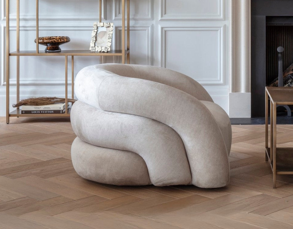 Modern living room with a curved beige sofa, gold bookshelf, and abstract art on the wall.