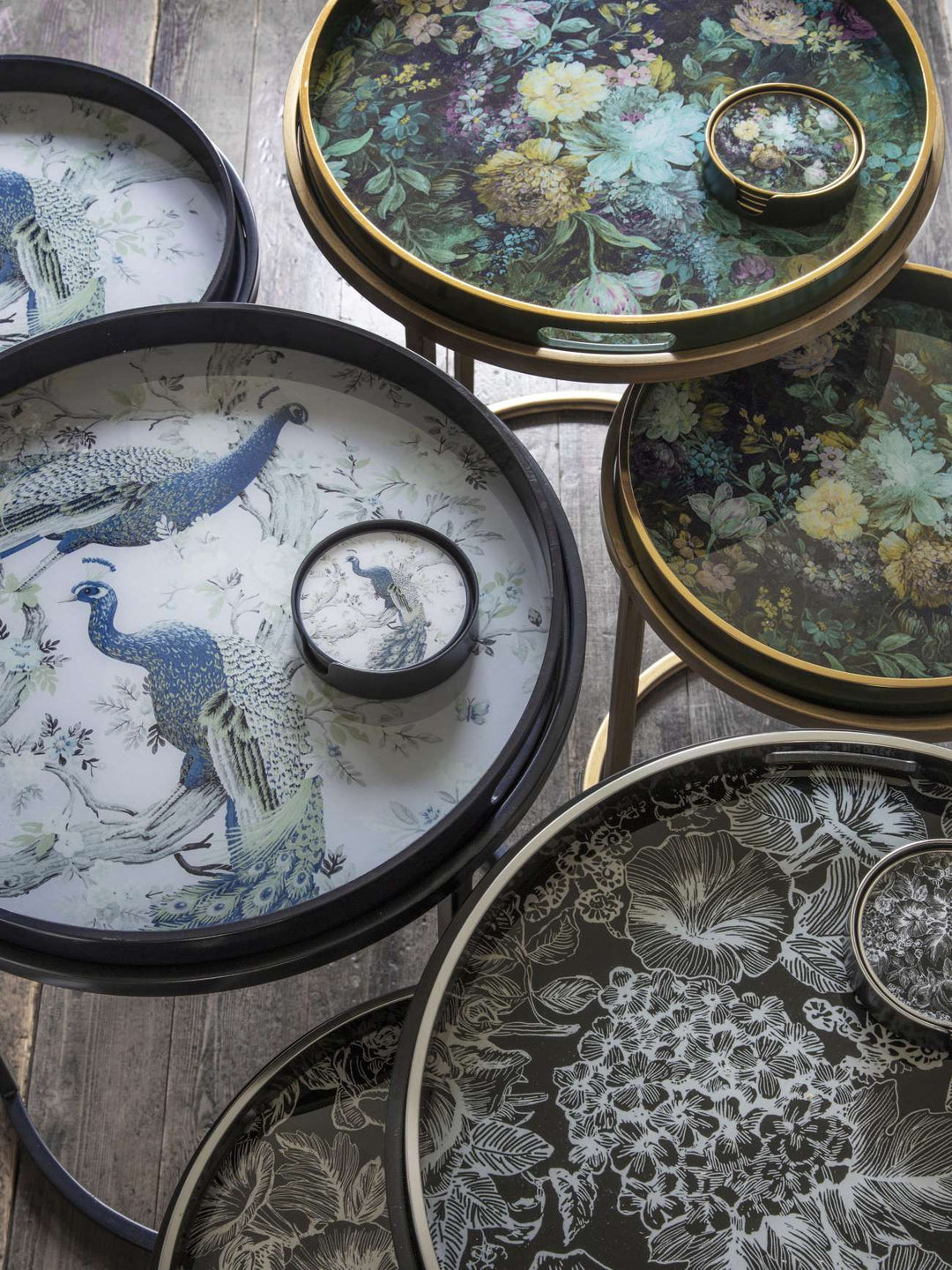Decorative trays with floral and peacock designs on a wooden surface