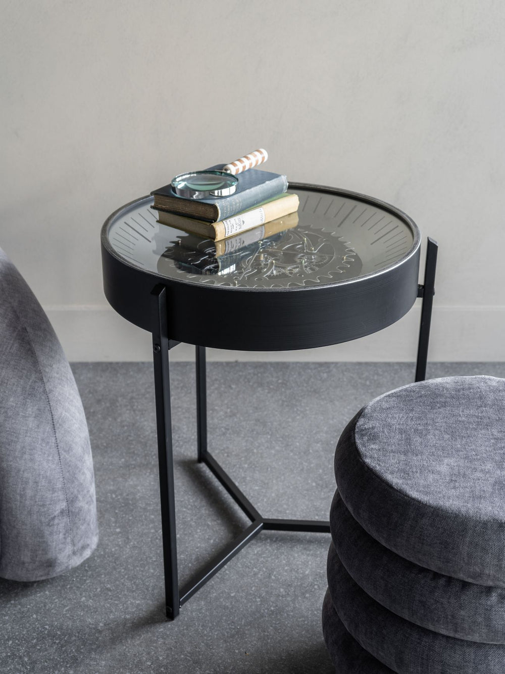Black round side table with books and a magnifying glass on a gray carpeted floor.