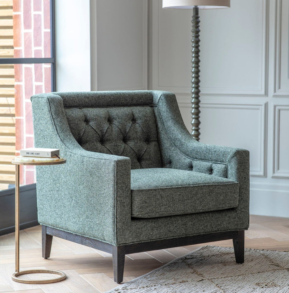 Gray upholstered armchair in a living room setting with a side table and lamp.