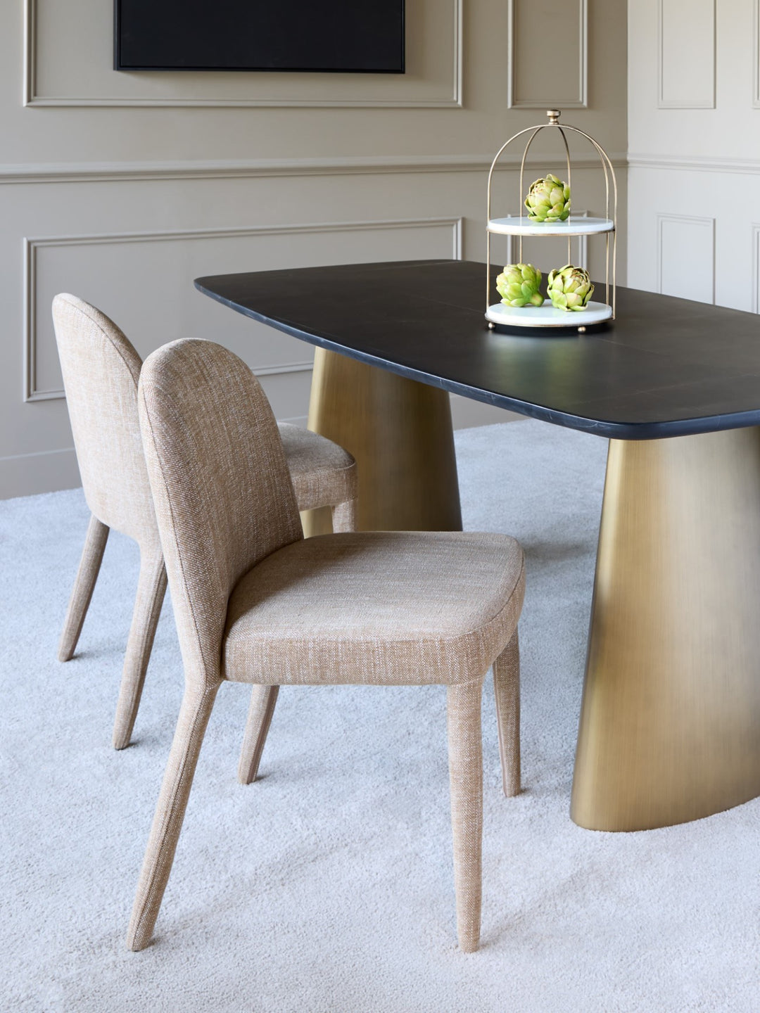 Dining room with a black and gold table and beige chairs.