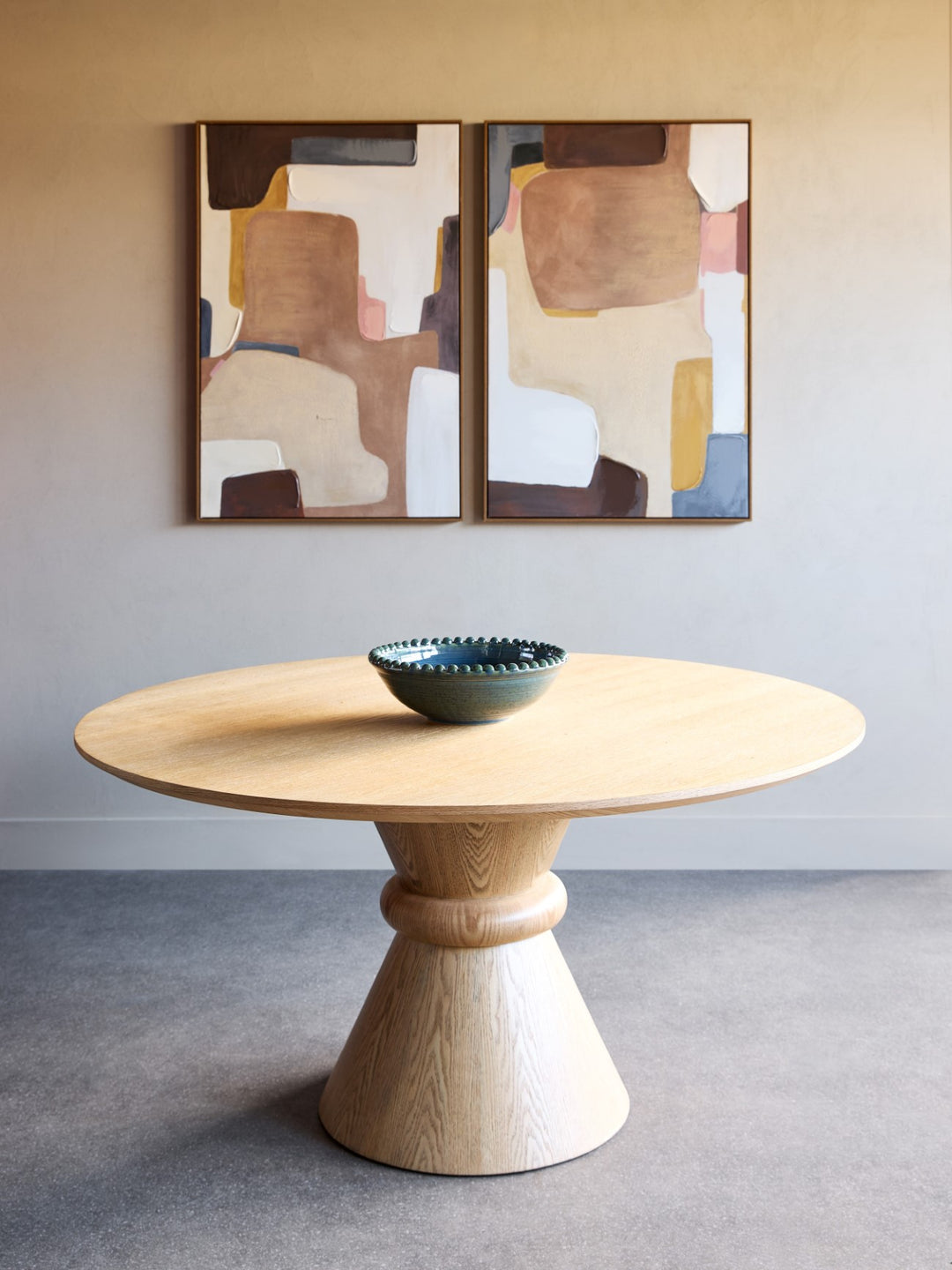 Wooden dining table with a bowl on top, against a wall with abstract art.